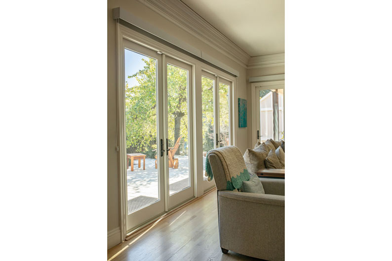 Interior view of a living room featuring large sliding glass doors leading to an outdoor patio with trees, designed by Alexander Company in Burlingame.